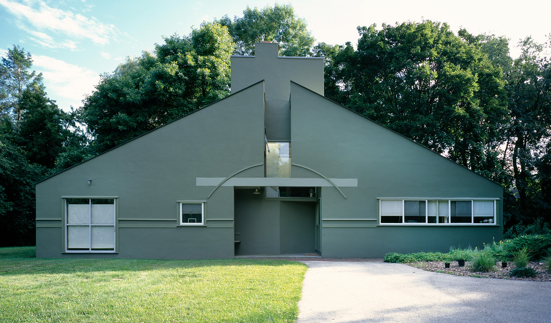 Relatively small house with a sloped roof, central chimney stack and non-structural arch above the entrance